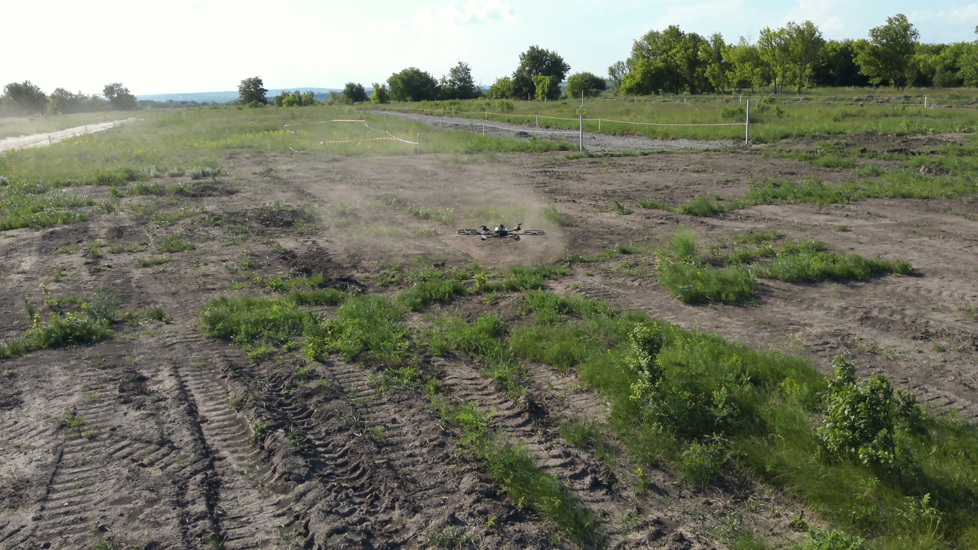 Ailand Systems drone hovering low over a patchy green field stirring up a small dust cloud