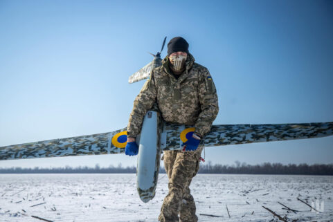 An operator carries a Ukrspecsystems UAV over snow-covered ground against a blue sky.