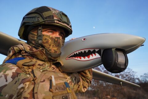 A Ukrainian soldier holds a Ukrspecsystems Shark UAV over his shoulder against a blue sky