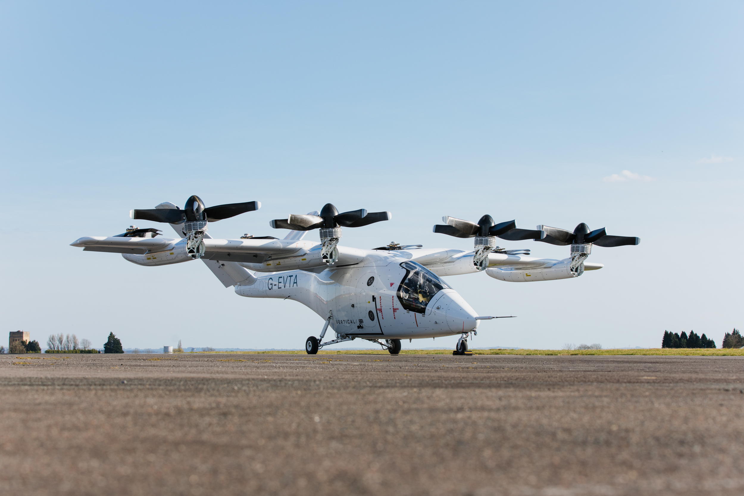 A white Vertical Aerospace VX4 eVTOL prototype sits on a paved surface against a pale blue sky